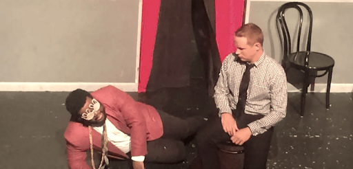 a man in a red blazer and gold chains lying on the phone next to a man in a shirt and tie